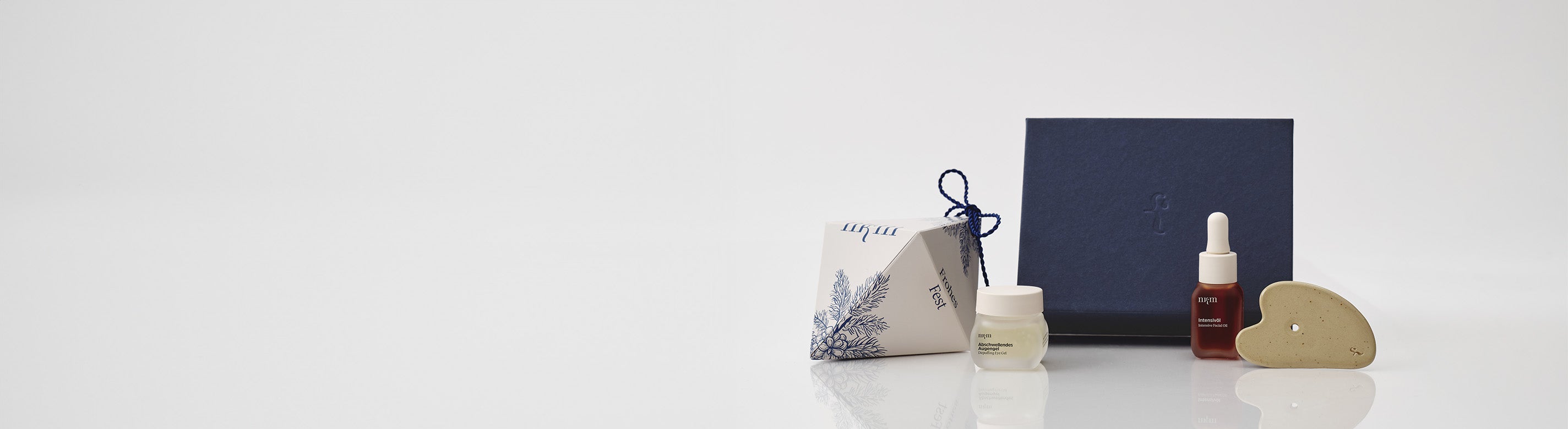 Weihnachtliches Ornament, blaue Geschenkbox und davor das Abschwellende Augengel, sowie das Intensivöl und der Gua Sha von nkm